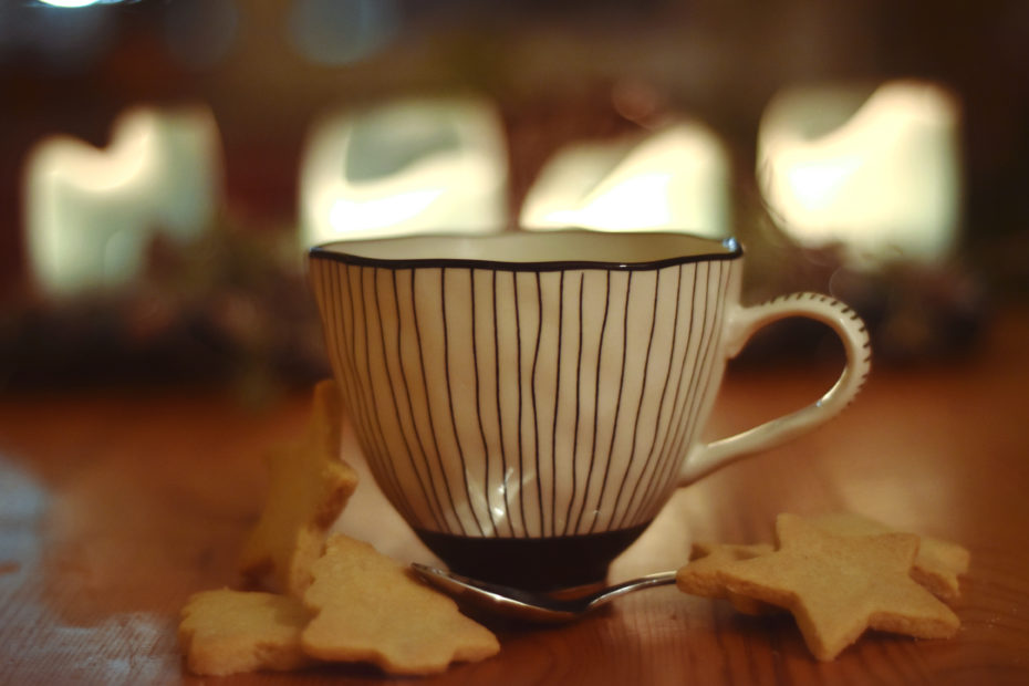 Eine Tasse Tee mit Plätzchen und Kerzen im Hintergrund